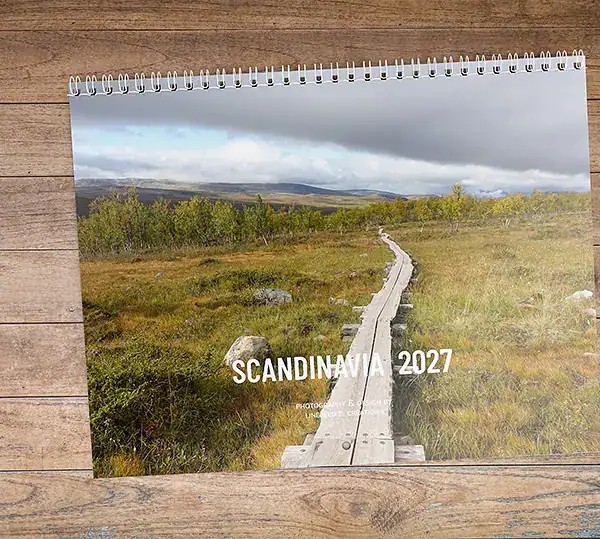 Scandinavië door de seizoenen 2027 fotokalender met een houten promenade die door het Scandinavische landschap loopt.